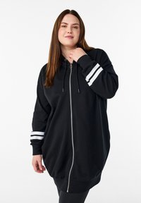 Melna kapuci džemperkleita ar rāvējslēdzēju un apaļu formu, ar baltām svītrām uz piedurknēm un kapuci ar auklu. Izgatavota no mīksta, teksturēta materiāla.