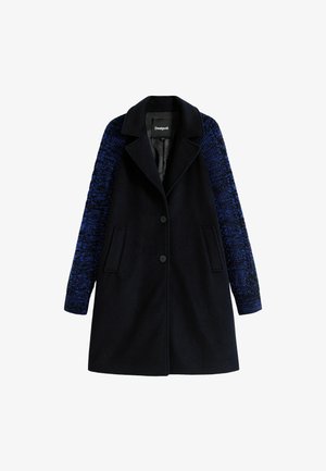 Marineblauw jasje met gestructureerde mouwstoffen in blauw, dubbele voorzakken, insnede kraag en zwarte knopen sluiting. Gevoerde binnenkant.