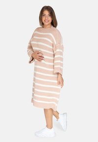 Strickkleid mit lockerer Passform, featuring horizontale beige und weiße Streifen, langen Ärmeln und einem runden Ausschnitt, kombiniert mit weißen Turnschuhen.