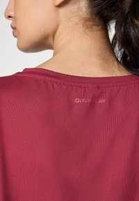Top sportivo bordeaux, texture liscia, con un collo a girocolla e orlo cucito, presenta un discreto branding "ONLY PLAY" sul retro.