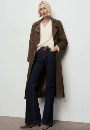 Abrigo largo de ante marrón sobre un suéter de punto blanco y suave, combinado con jeans oscuros acampanados y tacones marrones, con un cinturón ajustado.