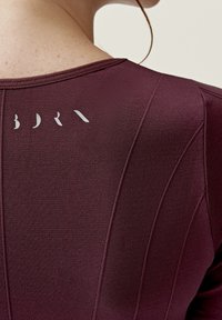 Burgundyröd atletisk topp med texturerad tyg, med vertikal sömnad och en subtil logotyp på baksidan i ljusgrått.