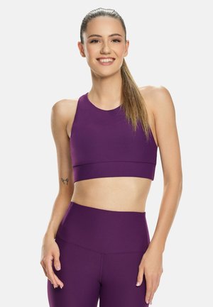 Reggiseno sportivo viola con scollo rotondo e spalline larghe, abbinato a leggings alti in vita dello stesso colore, in tessuto liscio e senza motivi visibili.