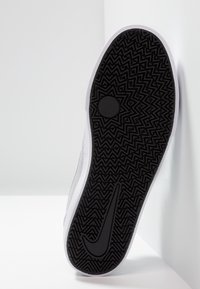 Svart gummiyttersula med zigzag-mönster, vit mellansula och mjukt grått övermaterial. Har Nike-logotyp på sidan.