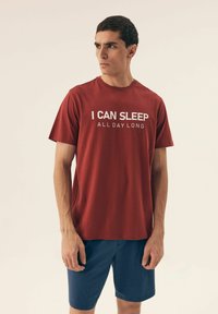 Czerwona bawełniana koszulka z krótkim rękawem i okrągłym dekoltem, z białym napisem: "MOGĘ SPAĆ CAŁY DZIEŃ." Połączona z granatowymi szortami.