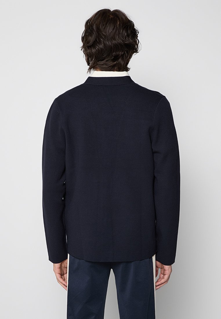 Marineblaue Jacke mit glatter Textur, taillierter Passform und klassischem Kragen. Verfügt über ein minimalistisches Design und keine sichtbaren Metallteile.