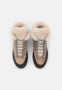 Bottes de randonnée beiges avec un col en fausse fourrure, des accessoires en métal argenté, une semelle noire et des lacets à motifs. Tige en matériau suédé.