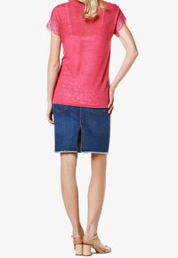 Top rosa con encaje en los bordes y mangas cortas; vista trasera de una falda de mezclilla azul con una hendidura central y dobladillo deshilachado, combinada con sandalias de tacón bloque en color nude.