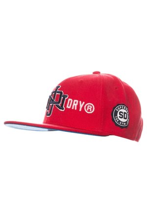 Rød kasket med flad skygge med sort og hvidt broderet logo og tekst "DRY®," samt et rundt sort mærke med "SUPERDRY SD TOK. GYM. JPN." på siden.