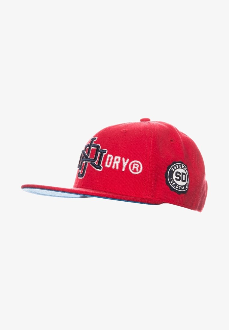 Casquette rouge à visière plate avec logo brodé en noir et blanc et le texte "DRY®," ainsi qu'un patch rond noir avec "SUPERDRY SD TOK. GYM. JPN." sur le côté.