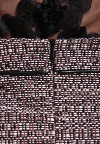 Texturovaná látka v vínové, černé a bílé tkané vzoru má černou květinovou výšivku na výstřihu s centrálním zipovým zapínáním.
