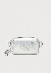 Geantă crossbody dreptunghiulară metalică argintie, cu logo-ul "ck" în relief și închidere cu fermoar. Dispune de o curea reglabilă și textură netedă din piele.