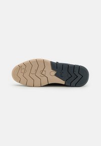 Semelle de chaussure avec un schéma de couleurs noir et beige, présentant un motif de semelle en zigzag, des accents texturés et un détail de logo en relief.