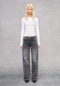 Witte lange mouwen fitted top, gecombineerd met losse, hoogwassende donkergrijze jeans. De jeans hebben vijf zakken en een subtiele vervaagde textuur.