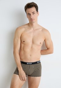 Schwarze und goldene gestreifte Boxershorts mit einem breiten elastischen Bund, auf dem der Markenname "BOSS" steht. Weicher Stoff und taillierte Passform.