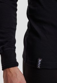 Schwarzes Langarmshirt aus Baumwolle mit tailliertem Design, gerippten Manschetten und einem kleinen Markenschild, das am Saum angenäht ist.