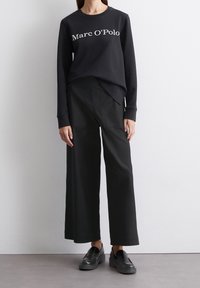 Czarny sweatshirt z białym napisem "Marc O'Polo", w połączeniu z szerokimi czarnymi spodniami i czarnymi butami na slip-on. Prosty design, luźny krój.
