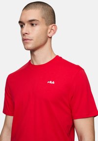 Rød kortærmet t-shirt lavet af bomuld, med rund halsudskæring og et lille hvidt Fila-logo på venstre bryst.