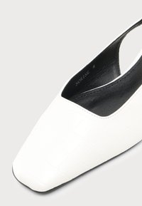 Chaussure slingback blanche avec doublure intérieure noire et motif carré subtil sur la tige, montrant un design à bout pointu.