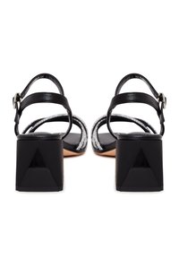 Schwarze Sandalen mit hohen Absätzen, zwei schlanken verstellbaren Riemen, einem strukturierten Fußbett und einem geometrischen Blockabsatz mit einer dreieckigen Akzentuierung.