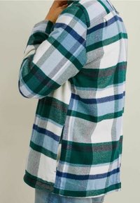Zielono-niebieska flanelowa koszula w kratę z białymi akcentami. Charakteryzuje się luźnym krojem, długimi rękawami i bocznymi rozcięciami dla swobody ruchów.