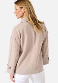 Helle beigefarbene Leinenjacke mit entspannter Passform, weitem Kragen und geknöpften Ärmelbündchen. Sie weist eine strukturierte Oberfläche und ein einfaches, minimalistisches Design auf.