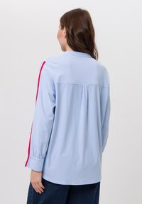 Blau-weiß gestreiftes Langarmhemd mit Kragen, das rosa Streifen entlang der Ärmel und ein lockeres Rückendesign aufweist.