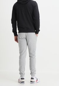 Felpa nera con cappuccio, pantaloni grigi da jogging e scarpe sportive. Materiali morbidi, design aderente e polsini elasticizzati con un aspetto pulito e casual.