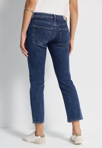 Jeans de mezclilla en azul oscuro con corte recto, que cuentan con bolsillos traseros y detalles de costura mínimos, combinados con zapatillas blancas.
