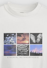 T-shirt branca de algodão com uma colagem de seis imagens: flores, pôr do sol, borboleta, paisagem, ondulações e floresta sob um céu noturno. Texto abaixo diz "METAMORFOSE ETÉREA."