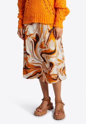 Oranje gebreide trui over een knielange rok met een oranje, zwarte en witte marmeren wervelpatroon. Bruine chunky sandalen met bandjes.