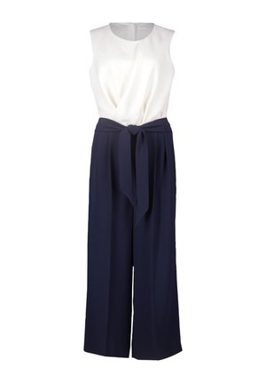 Hvid ærmeløs top med en knude detalje i taljen, parret med marineblå vide bukser lavet af et glat, vævet stof.
