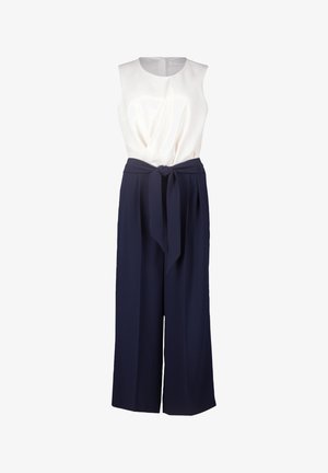 Hvid ærmeløs top med en knude detalje i taljen, parret med marineblå vide bukser lavet af et glat, vævet stof.