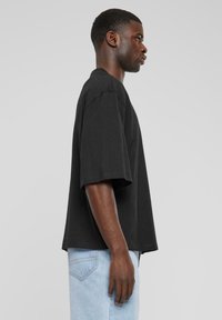 Black oversized t-shirt made of cotton, featuring short sleeves and a straight cut. Worn with light blue denim jeans. Simple design.