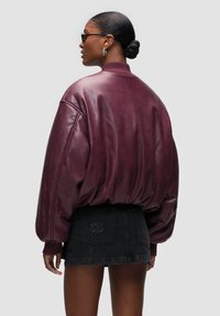 Bomber bunda z vínové kůže s žebrovanými manžetami, volným střihem a hladkou texturou, kombinovaná s černou denimovou sukní s vyšívaným logem.