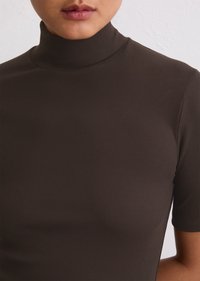 Col roulé marron à côtes avec des manches courtes, présentant un design ajusté et une texture lisse.