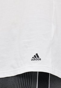 Fehér pamut póló, bal alsó sarokban fekete Adidas logóval. Az anyag sima tapintású, lazább szabással.