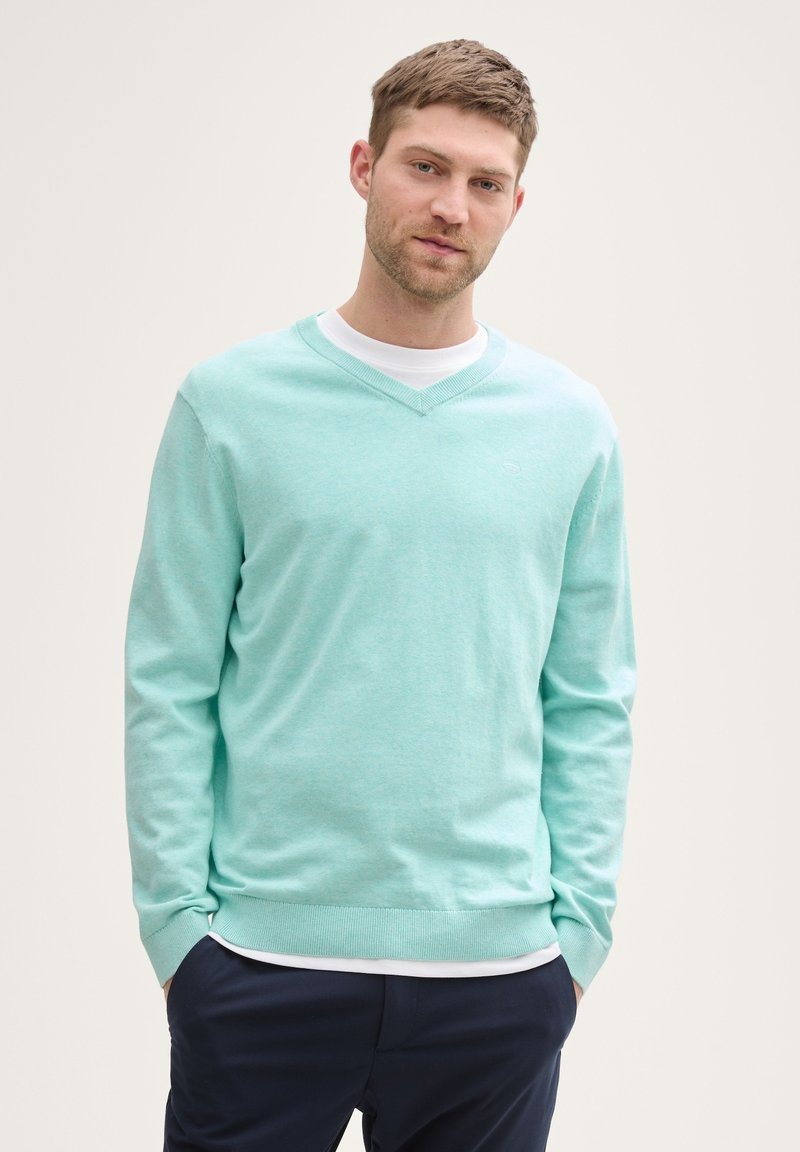 Licht mintgroene v-hals trui gemaakt van zachte katoen, met lange mouwen en geribde cuffs, gedragen over een wit shirt.