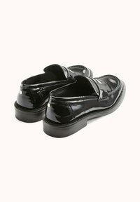 Mocassins en cuir verni noir avec un bout arrondi et un petit talon. Présentent des détails cousus et un petit accent sur le talon.