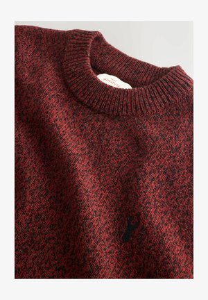 Lähikuva punaisesta ja mustasta neulotusta villapaidasta, jossa on ribbauskangas ja pieni musta hirvi-logo rinnassa.