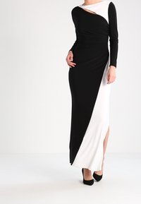 Lång klänning med svart och vit färgblockdesign, med en diagonal sprund och långa ärmar. Slät tyg med en sidoflik.