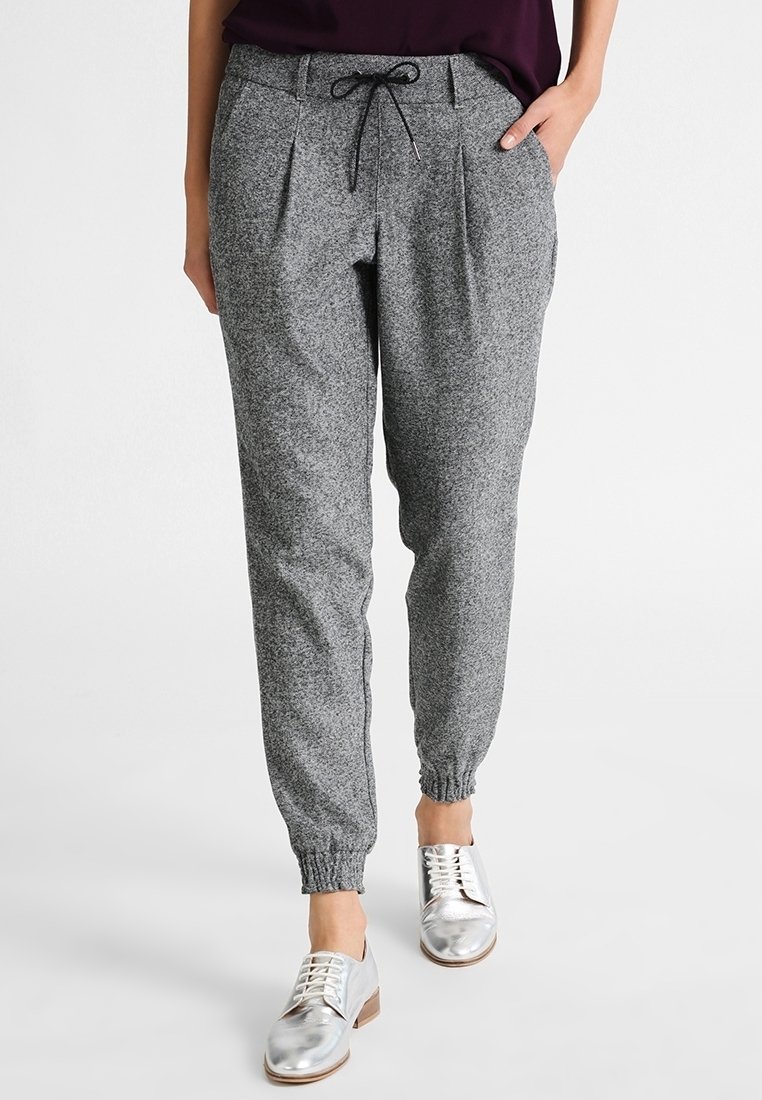 Pantalon de jogging gris à cordon avec plis et poignets élastiques, porté avec des chaussures à lacets argentées métalliques et un haut sombre.
