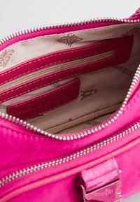 Interno di una borsa fucsia con tessuto morbido, dotato di una tasca con zip, una tasca a scomparsa e etichette. Visibili dettagli in metallo argentato e cuciture.