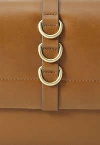 Sac en cuir marron avec une texture lisse, comportant trois boucles en métal doré et une bandoulière assortie. Couture soignée sur la surface.