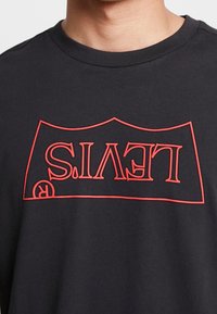 Camiseta negra con un logo de Levi's en contorno rojo colocado al revés en la parte frontal. Tejido suave con un diseño de cuello redondo.