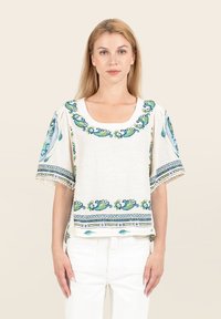 Top bianco a maniche corte con ricami floreali blu e verdi. Scollatura quadrata, vestibilità comoda, rifiniture decorative lungo le maniche e l'orlo.