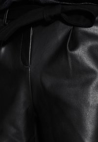 Czarne skórzane spodnie o gładkiej fakturze, z plisowanym wzorem i materiałowym paskiem zawiązanym w pasie.