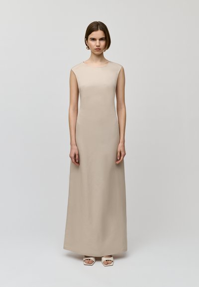 Abito maxi beige senza maniche con una texture liscia e morbida. Design semplice con scollatura rotonda. Indossato con sandali con tacco a blocco e punta aperta.