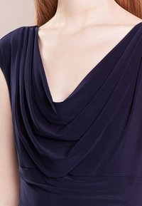 Námořnické šaty s draped cowl výstřihem a měkkou, texturovanou tkaninou. Obsahují na ramenou detail s nařasením a přiléhavý pas.