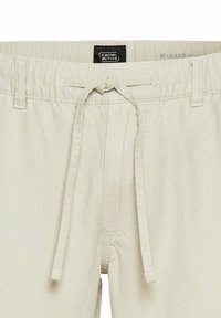 Lys beige, afslappede shorts med elastisk talje og snor. Lavet af et tekstureret, åndbart stof. Brandmærket er synligt.